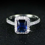 Silver women's engagement ring with rectangular blue sapphire and surrounding small diamonds in prong setting