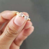Close-up of a Princess Zircon Gold Ring with bowknot design, 18k gold plated and bezel set zircon stones, held between fingers.