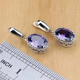 Pair of silver earrings with oval purple amethyst gemstones next to a ruler for size reference