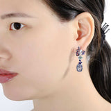 Close-up of woman wearing luxury flower amethyst dangling earrings in 925 sterling silver with purple enamel accents.