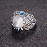 Vintage opal cat eye ring with hollow silver feather design and blue stone accents on textured background