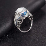 Vintage opal cat eye ring with hollow silver feather design and blue gemstone accents on black textured background