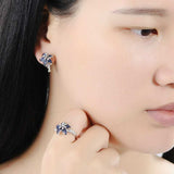 Woman wearing luxury gem flower jewelry set with blue and white zircon 925 sterling silver ring and matching earrings