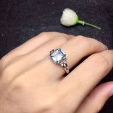 Natural blue aquamarine ring with oval cut stone and sterling silver prong setting on woman's hand.