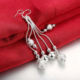 Long silver dangle earrings with multiple chains and spherical accents on red fabric background