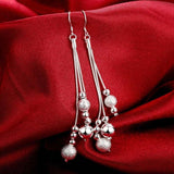 Long silver dangle earrings with multiple silver beads on red fabric background