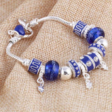 Silver charm bracelet with blue beads and dangling charms on textured fabric background