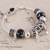Silver charm bracelet with black and silver beads on a textured surface